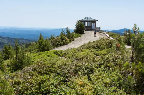 A small cabin sits on a mountain ridge overlooking a hazy landscape.
