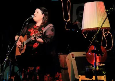 A woman singing and playing acoustic guitar indoors.