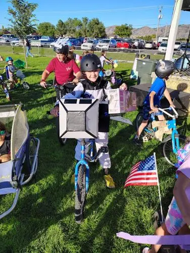 Children with decorated bicycles gather on the grass.
