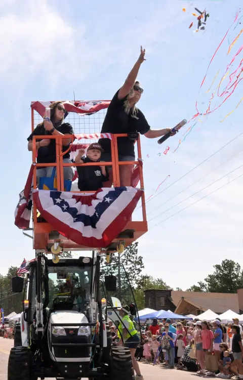 People ride on a decorated lift during a parade, throwing confetti and streamers to the crowd.