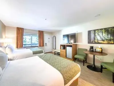 A hotel room interior with two beds, a desk, and chairs.