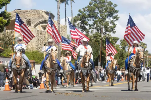 A group of horseback riders carrying American flags participate in a parade.