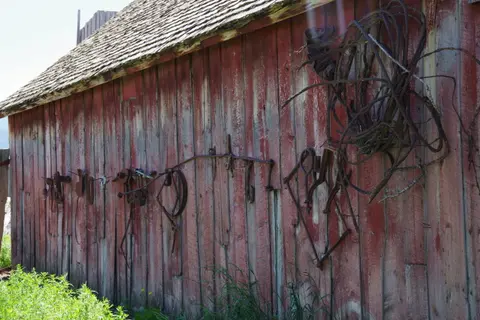 A weathered red barn exterior with old farm equipment hanging on its wall.