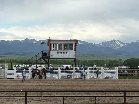 A rodeo arena with a judge's stand and mountains in the background.