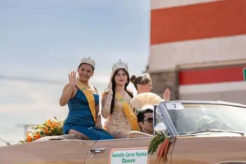 People waving from a convertible car during a parade.