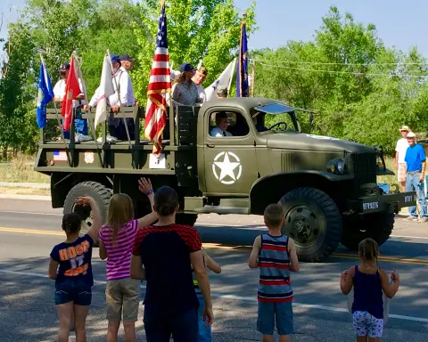 People watch a military truck with flags on the bed drive by in a parade.