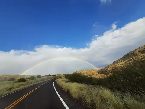 A rainbow stretches across the sky above a winding road and hills.