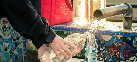 Water is poured from a metal spout into plastic bottles.