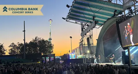 A crowd watches a concert performance on an outdoor stage at dusk.