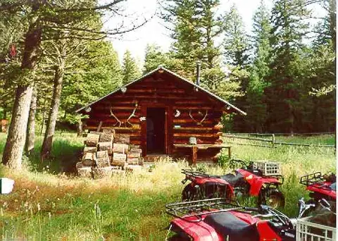 A log cabin in a wooded area with ATVs parked in the foreground.
