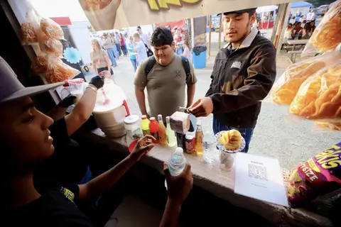 People buying food and drinks at an outdoor food stand.