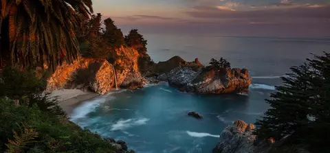 A scenic view of a coastal cove with a waterfall at sunset.