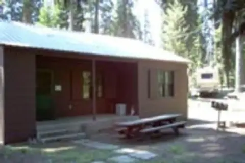 A small cabin in a wooded area with a picnic table outside.