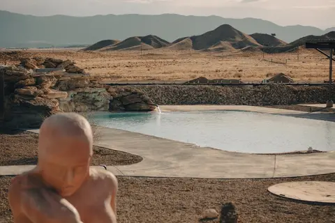 An outdoor pool in a desert landscape with a statue in the foreground.