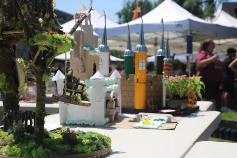 Handmade model castles and miniature tree displays sit on a table outside.