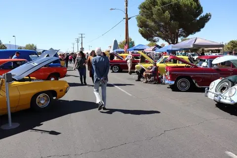 A car show takes place outdoors with various classic cars on display and people walking around.