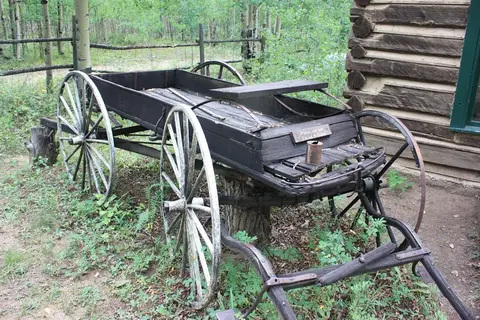 An old wooden wagon parked next to a log cabin.