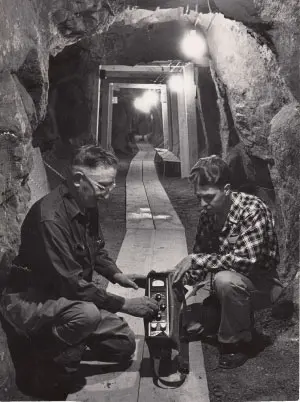 Black and white historic photo of two men operating equipment in a tunnel.