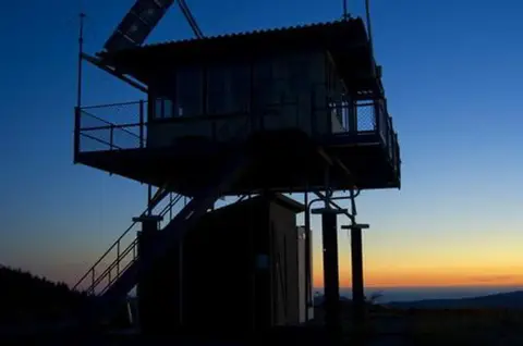 A fire lookout tower stands silhouette against a sunset sky.