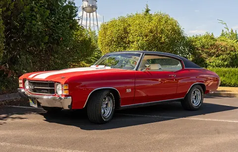 A red vintage muscle car parked in a paved lot.