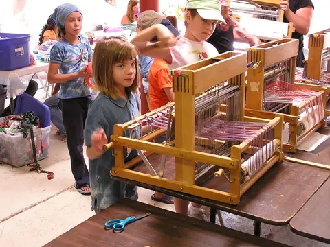 Children learn to weave on small wooden looms indoors.
