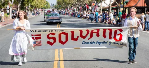 Two people carry a banner in a parade on a sunny street.