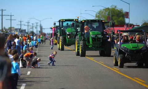 A parade featuring tractors and utility vehicles traveling down a street lined with spectators.
