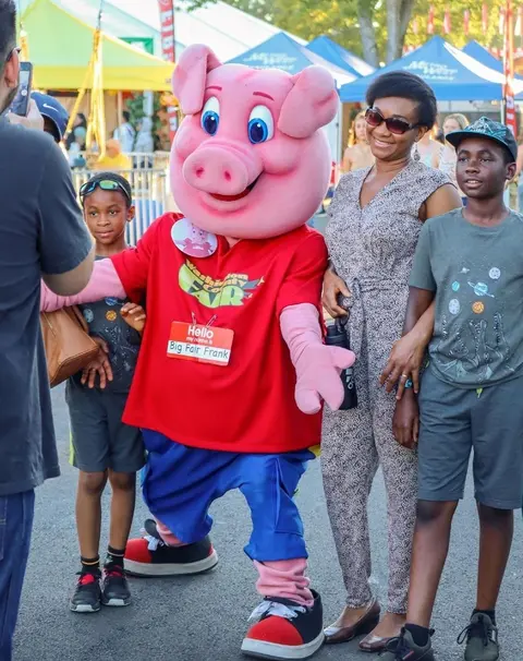 A pig mascot poses for a photo with a family at an event.