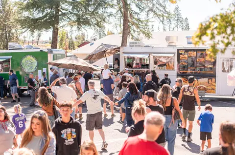 A crowd of people ordering food from food trucks outdoors.