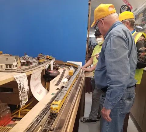 People look at a model train layout indoors.
