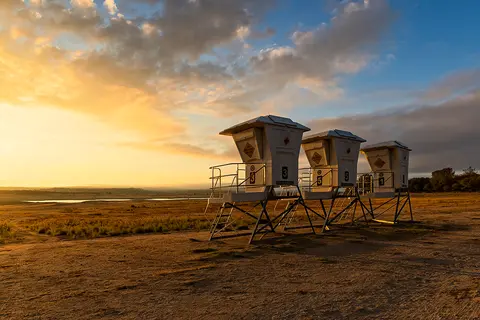 Three lifeguard towers stand on dry ground under a cloudy sunset sky.