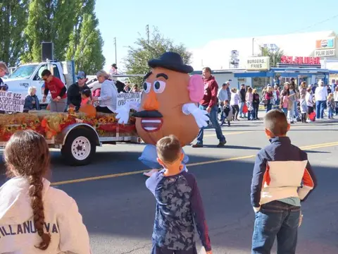 A large potato mascot walks in a street parade past spectators.