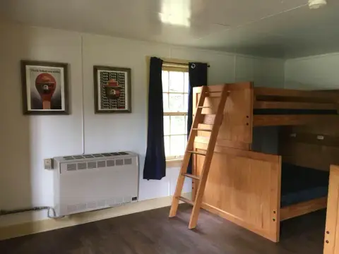 An interior view of a room with a wooden bunk bed, a window with dark curtains, and framed posters on the wall.