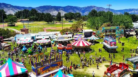 An elevated view of a carnival setup with tents, rides, and mountains in the background.