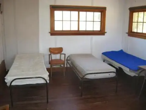 An interior view of a room with three single beds and a chair.