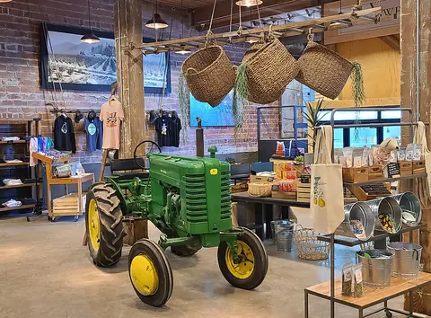 Interior view of a rustic retail space featuring a vintage green tractor, hanging baskets, and merchandise displays.