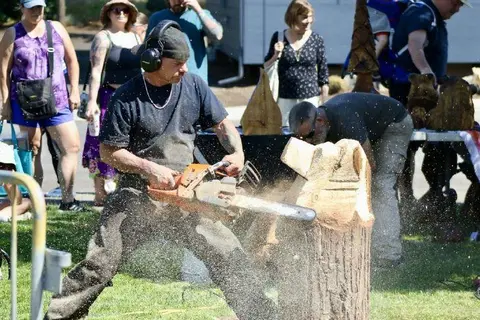 A man uses a chainsaw to carve wood outdoors while people watch.
