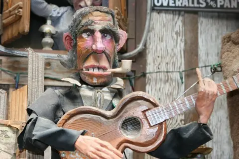 A wooden automaton figure holding a guitar and smoking a pipe.