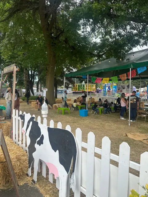 An outdoor family event with a decorated tent, a fence with a cow cutout, and people enjoying activities.