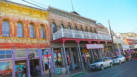 Historic storefronts line a street with cars parked along the curb.