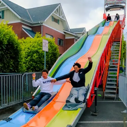 People go down a large multi-lane slide at a fair.