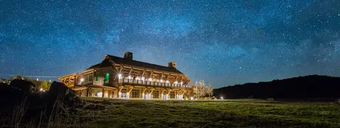 A wooden lodge stands under a starry night sky.