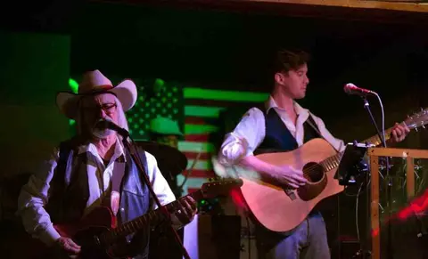 Two musicians playing guitars on stage indoors.