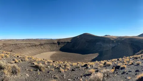 A wide-angle landscape view of a large volcanic crater in an arid desert environment.