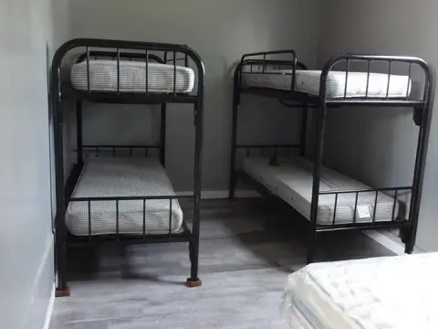 A bedroom with two black metal bunk beds and a mattress in the foreground.