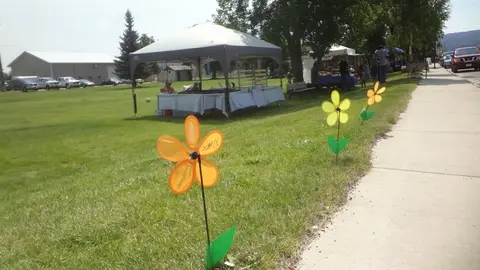 An outdoor market or event setup with tents and flower pinwheels along a sidewalk.