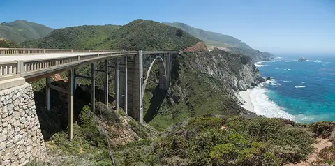A bridge spans across a coastal valley next to the ocean.