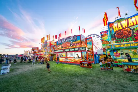 A row of colorful food stands at an outdoor fair.