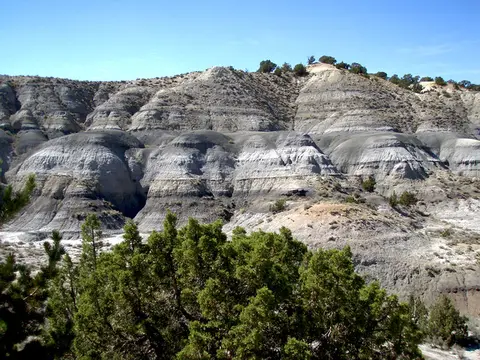 A landscape photograph showing banded clay hills and sparse vegetation under a clear blue sky.