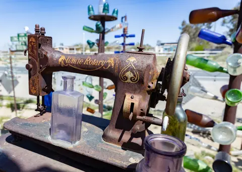 A rusty vintage sewing machine sits outdoors with glass bottles around it.